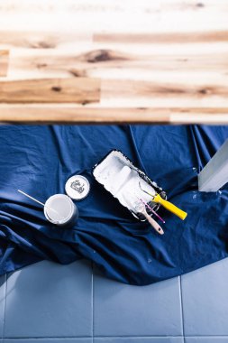 Boya tepsisi silindirli bir tencere beyaz boya ve mavi çarşafın üstünde fırçalar. Tabloyu boyamaya hazır. Boya kutusuyla sığ bir alanda çekilmiş.