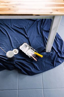 Boya tepsisi silindirli bir tencere beyaz boya ve mavi çarşafın üstünde fırçalar. Tabloyu boyamaya hazır. Boya kutusuyla sığ bir alanda çekilmiş.