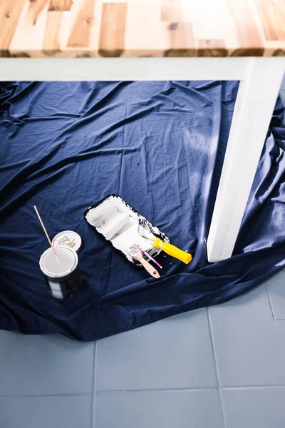 Boya tepsisi silindirli bir tencere beyaz boya ve mavi çarşafın üstünde fırçalar. Tabloyu boyamaya hazır. Boya kutusuyla sığ bir alanda çekilmiş.