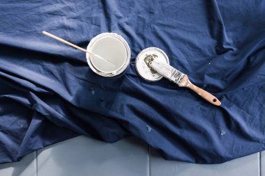 Mavi çarşafın üzerinde fırçayla boyanmış bir tencere beyaz boya. Boyaya hazır. Boya kutusuyla sığ bir alan derinliğinde çekilmiş.