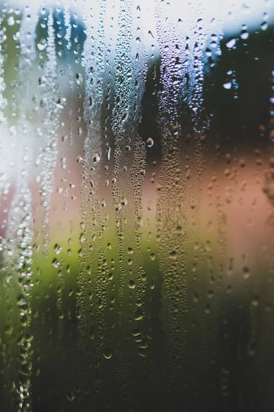 water droplets of humidity condensation on window seen from indoor with backyard bokeh in the background shot with a macro lens