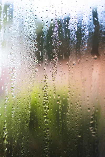 water droplets of humidity condensation on window seen from indoor with backyard bokeh in the background shot with a macro lens