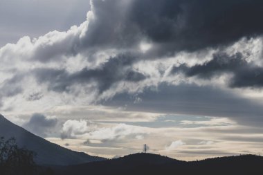 Yoğun güneş ışığıyla dağların üzerinden geçen yoğun fırtınalı bulutlar Tazmanya, Avustralya 'da kışın çekilen zıt tonlarda.