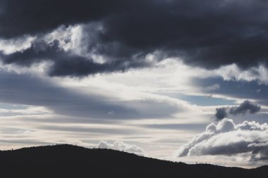 Yoğun güneş ışığıyla dağların üzerinden geçen yoğun fırtınalı bulutlar Tazmanya, Avustralya 'da kışın çekilen zıt tonlarda.
