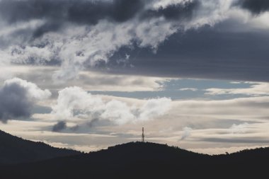 Yoğun güneş ışığıyla dağların üzerinden geçen yoğun fırtınalı bulutlar Tazmanya, Avustralya 'da kışın çekilen zıt tonlarda.