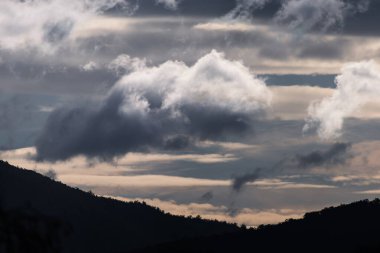 Yoğun güneş ışığıyla dağların üzerinden geçen yoğun fırtınalı bulutlar Tazmanya, Avustralya 'da kışın çekilen zıt tonlarda.