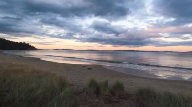 sunset on pristine beach in Southern Tasmania in Australia with colorful clouds reflecting over the Pacific Ocean and no people, shot in winter