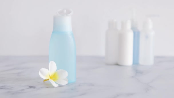 低毒性で毒性のない天然美品のコンセプトイメージ 他のボトルのグループから際立っている前景に青い化粧水ボトルの前に花を置く手 — ストック動画