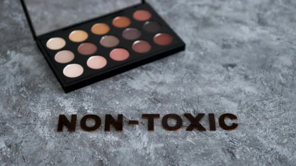 低毒性で自然な美しさの製品の概念的なイメージ 灰色の背景に毒性のないテキストを持つ化粧パレット — ストック動画