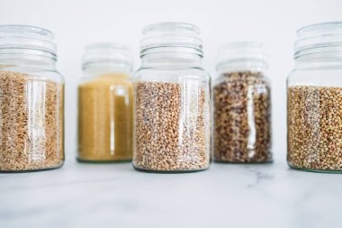 İçinde kinoa pirinç karabuğday kuskusu ve arpa da dahil olmak üzere içinde farklı tahıl türleri bulunan temiz kiler kavanozları, basit doğal sağlıklı bileşenler kavramı.