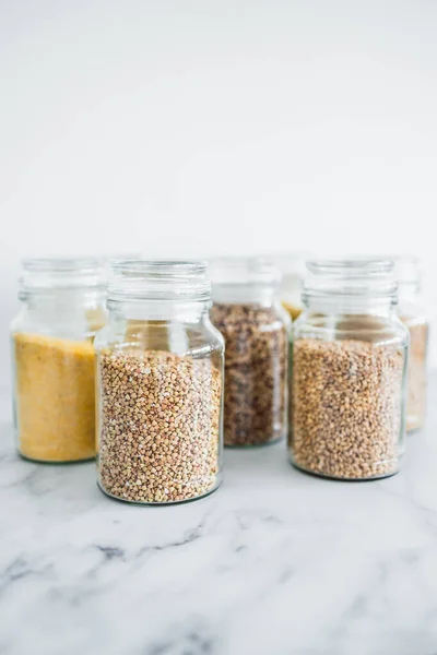 clear pantry jars with different types of grains in them including quinoa rice buckwheat couscous and barley, concept of simple natural healthy ingredients