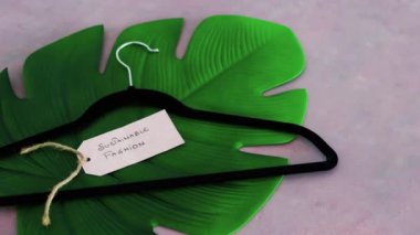 Elbise askısıyla sürdürülebilir moda etiketi pembe arka planda tropik yeşil yaprağın üzerinde sığ alan derinliğinde çekim, çevreye duyarlı giyim markaları kavramı