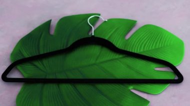 Elbise askısıyla sürdürülebilir moda etiketi pembe arka planda tropik yeşil yaprağın üzerinde sığ alan derinliğinde çekim, çevreye duyarlı giyim markaları kavramı