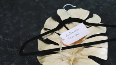 Giysi askısı ile sürdürülebilir moda etiketi altın yaprağın üzerinde siyah arkaplan üzerinde sığ alan derinliğinde çekim, çevreye duyarlı giyim markaları kavramı