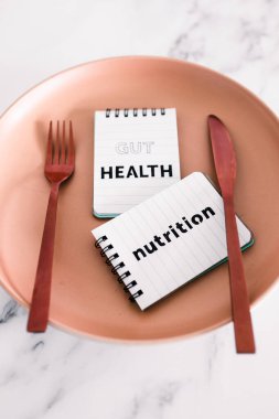 Yemek tabağının tepesindeki not defterlerinde çatal ve bıçakla beslenme metni, sağlıklı beslenme kavramı ve bilimsel araştırma.