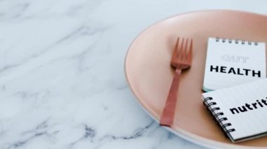 Yemek tabağının tepesindeki not defterlerinde çatal ve bıçakla beslenme metni, sağlıklı beslenme kavramı ve bilimsel araştırma.