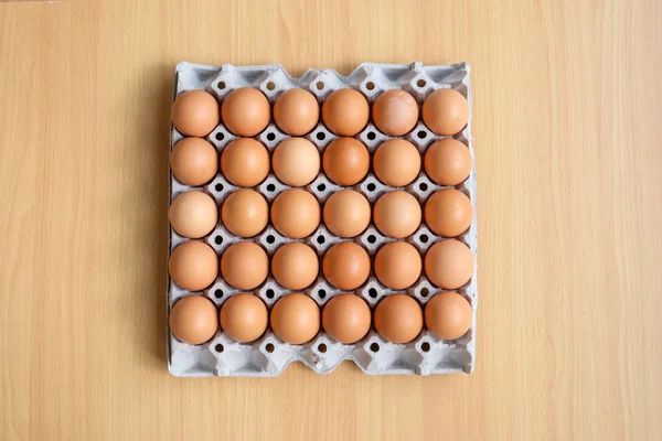 Uma dúzia de ovos marrons em uma caixa em uma mesa de madeira — Fotografia de Stock