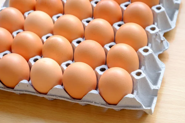 Kilkunastu brązowe jaja w kartonie na drewnianym stołem — Zdjęcie stockowe