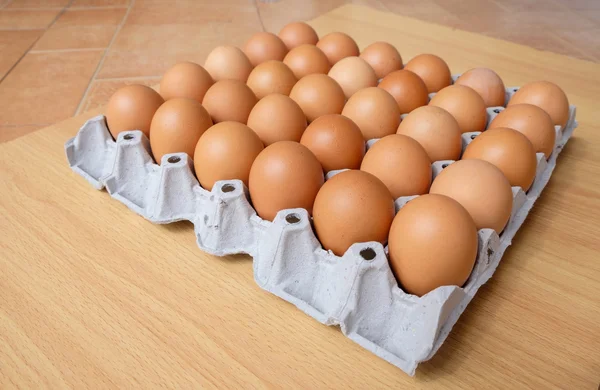 Uma dúzia de ovos marrons em uma caixa em uma mesa de madeira — Fotografia de Stock