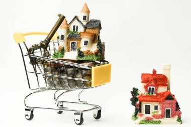 Alışveriş arabasındaki bozuk paraların üzerinde anahtar olan küçük bir ev. Beyaz arka planda izole edilmiş. kavram fikirleri. kopya alanı, satış ve emlak alımı 