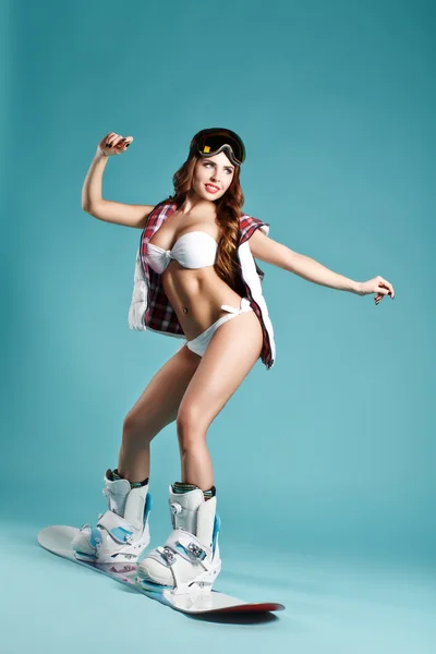 Eerste keer aan boord. Aantrekkelijke jonge Sexy meisje in Bikini evenwicht houden op Snowboard op blauwe achtergrond. Studiofotografie. Ideaal voor advertentie — Stockfoto