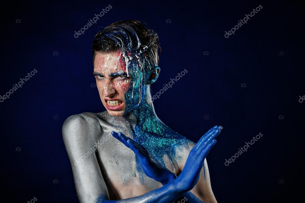 Crazy young androgyne man with face art. Freak person. Sperm on face. Tinsel creative blue makeup. Intersex and homosexuality concept. Space for logo
