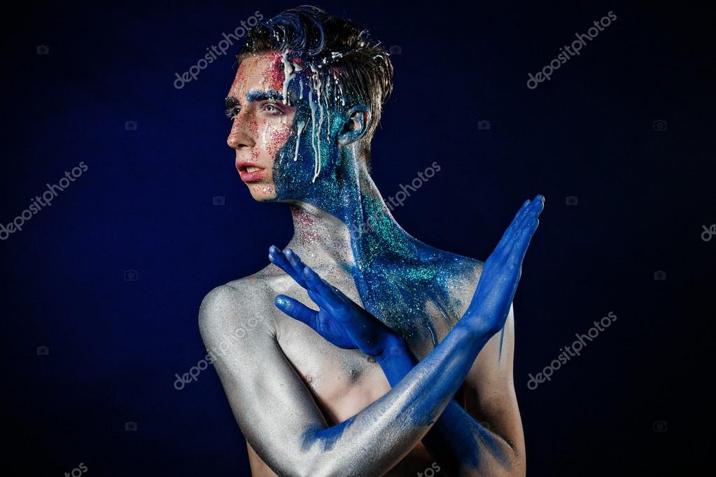 Crazy young androgyne man with face art. Freak person. Sperm on face. Tinsel creative blue makeup. Intersex and homosexuality concept. Space for logo