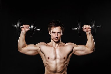Handsome athletic man with dumbbells confidently looking forward