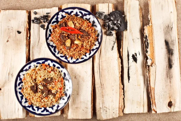 Traditionelles zentralasiatisches Pilaw in usbekischer Platte auf Baumstämmen — Stockfoto