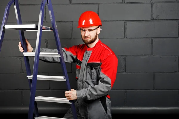 Portrait of man wearing overalls with step ladder near brick wal Stock Image