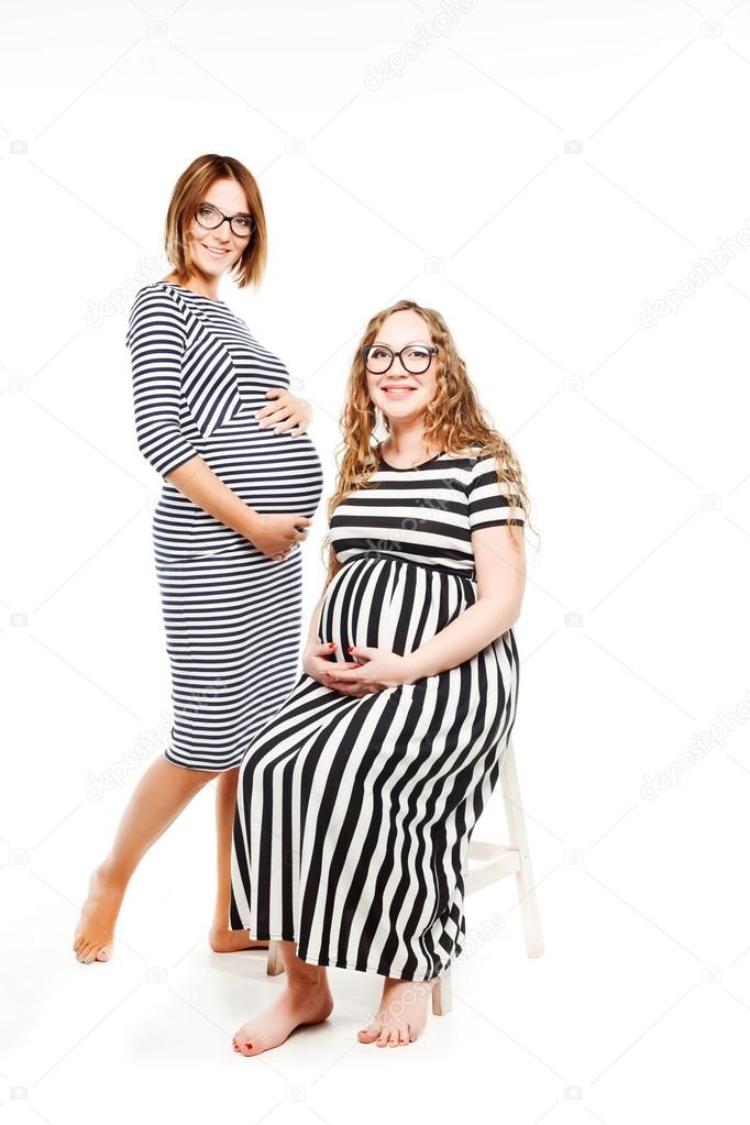 two happy pregnant women is glasses touch their belly