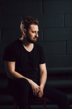 Handsome bearded men in black shirt thinking about his life near brick wall