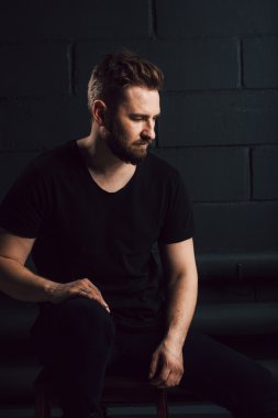 Handsome bearded men in black shirt thinking about his life near brick wall