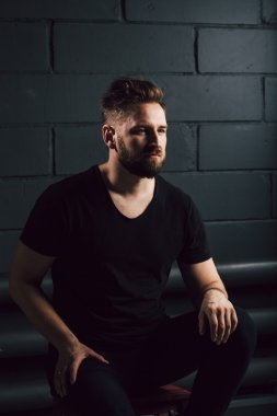 Handsome bearded men in black shirt thinking about his life near brick wall