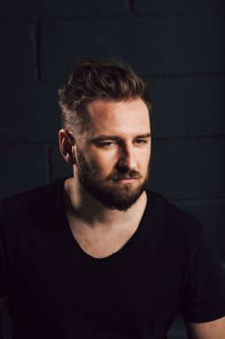 Handsome bearded men in black shirt thinking about his life near brick wall
