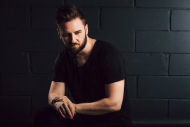 Handsome bearded men in black shirt thinking about his life near brick wall