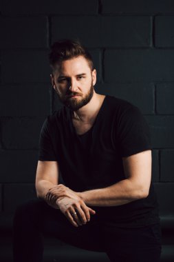 Handsome bearded men in black shirt thinking about his life near brick wall