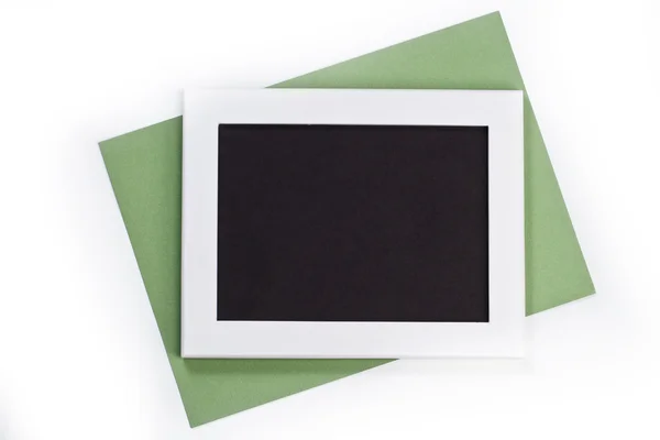 Marco de fotos blanco horizontal con campo negro y papel verde bajo ángulo sobre fondo blanco aislado con sombras reales — Foto de Stock