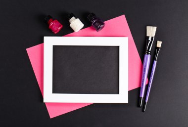 black and pink template with white photo frame on pink paper with brushes and gouache. Painter workplace