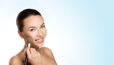 young beautiful brunette woman with nude makeup smile and hold brush at face. naturalness isolated photo with blue gradient.
