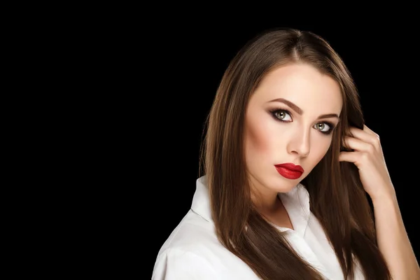 Young beautiful brunette woman with makeup and red lips in white shirt touch her hairs on black background — Zdjęcie stockowe