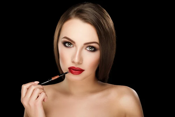 Young beautiful brunette woman with makeup and red lips apply lipstick on black background — Stok fotoğraf