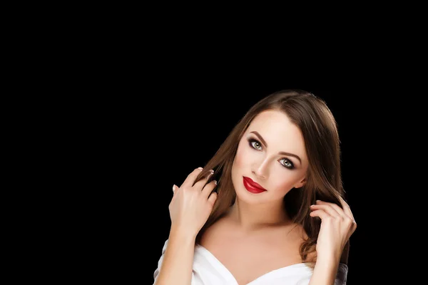 Young beautiful brunette woman with makeup and red lips in white shirt touch her hairs on black background — Stok fotoğraf