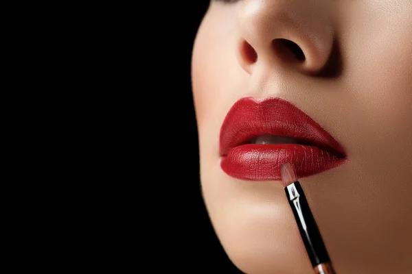 Nahaufnahme Makro-Foto von Pinsel mit Lippenstift und natürliche große rote Lippen der jungen Frau auf schwarzem Hintergrund — Stockfoto