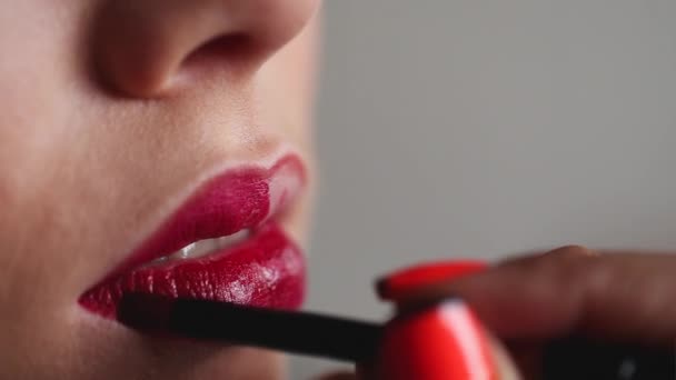 Closeup θέα προς το επαγγελματίας καλλιτέχνης μακιγιάζ είναι εφαρμόζοντας κόκκινο lip gloss για ένα νεαρό κορίτσι Καυκάσιος μοντέλο με ωραίο δέρμα — Αρχείο Βίντεο
