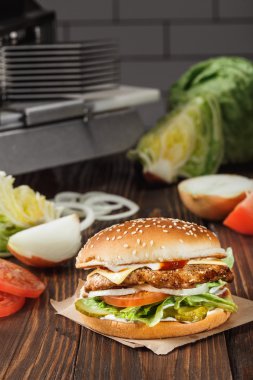 Peynirli hamburger ızgara et, peynir, domates, sebze arasında mutfak ahşap yüzey üzerinde Kraft kağıt üzerinde. Fast food şablonu.