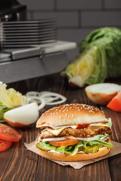 Hambúrguer de queijo com carne grelhada, queijo, tomate, no papel de ofício na superfície de madeira na cozinha entre verduras. Modelo de fast food . — Fotografia de Stock