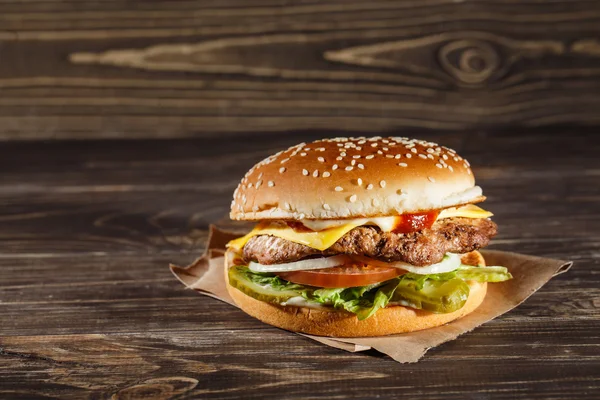 Sabrosa hamburguesa de queso con carne a la parrilla, queso, tomate, sobre papel artesanal en la superficie de madera. Plantilla de comida rápida . — Foto de Stock