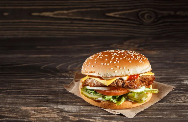 Νόστιμο burger τυριών με ψητό κρέας, τυρί, ντομάτα, σε χαρτί βιοτεχνίας στην ξύλινη επιφάνεια. Πρότυπο Φάστ φούντ. — Φωτογραφία Αρχείου