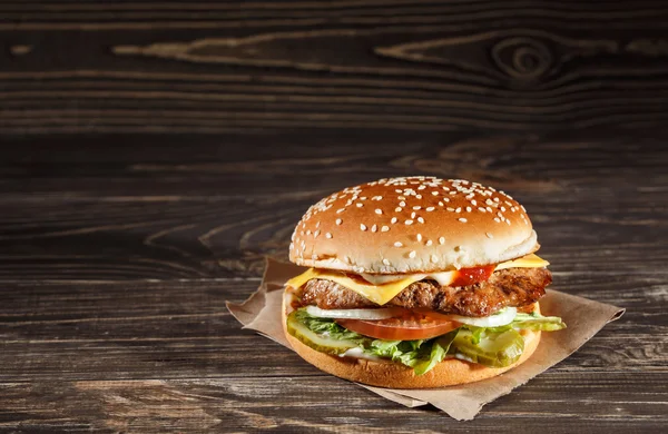 Tasty Cheese burger with grilled meat, cheese, tomato, on craft paper on wooden surface. Fast food template. — Stock Photo, Image